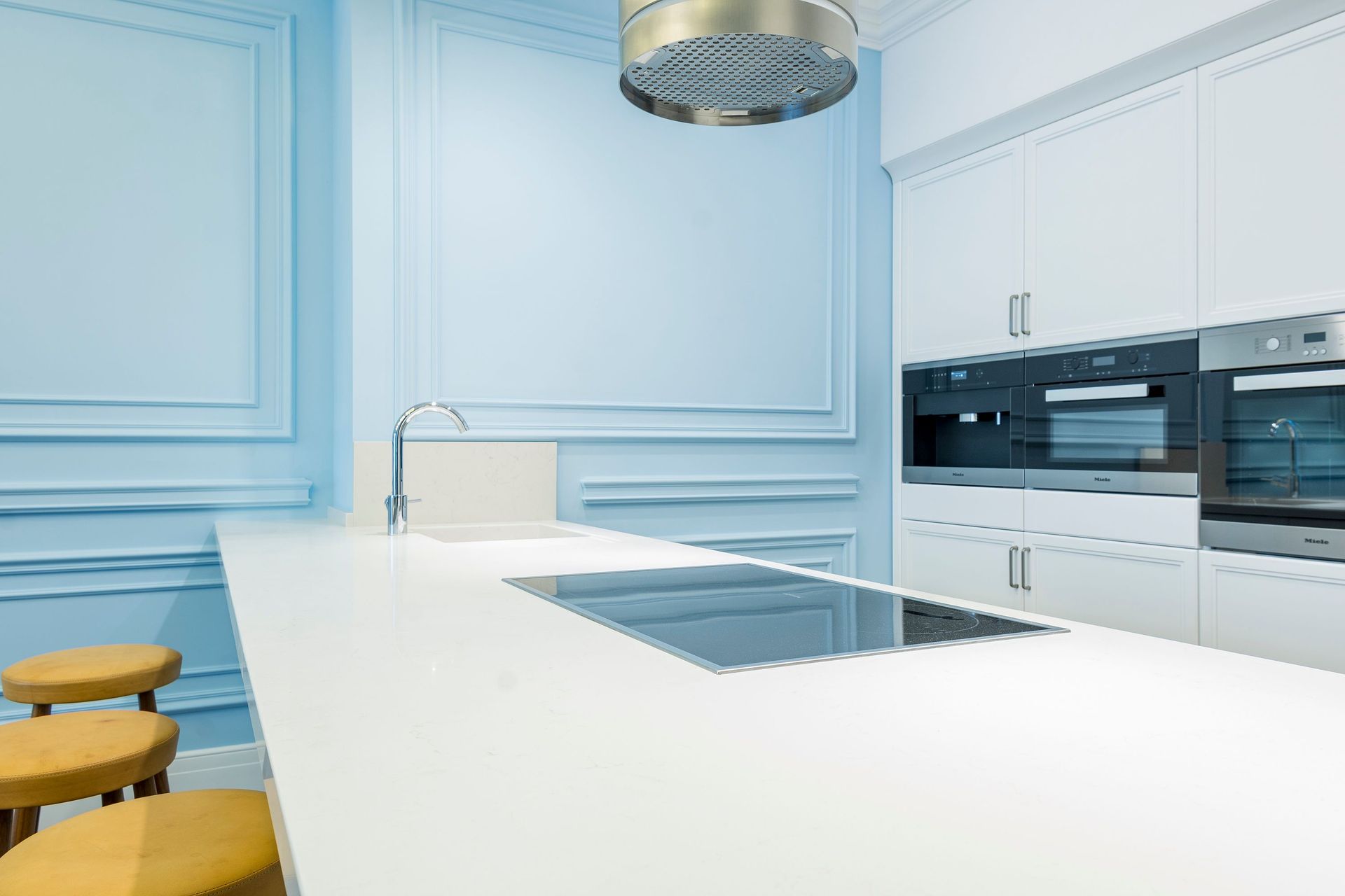 Bright, modern kitchen with minimalist design featuring blue walls and sleek white countertops.